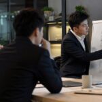 Ein junger Consultant präsentiert vor einem Team, während im Hintergrund digitale Dashboards und KI-Symbole den Einfluss von Automatisierung auf die Beratung visualisieren