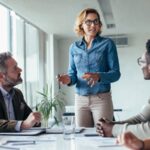 Professionelles Business-Beitragsbild: Zwei junge Consultants diskutieren vor einer digitalen Tafel, die Geschäftsprozesse und KI-Symbole zeigt