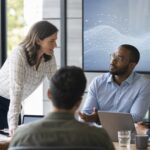 Professionelles Business-Bild: Eine Führungskraft im Beratungsumfeld, die mit ihrem Team vor einem digitalen Dashboard mit KI-Analysen steht und gemeinsam Strategien diskutiert