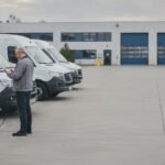 Fuhrpark eines mittelstaendischen Betriebs: Transporter am Ladepunkt, Fuhrparkleitung prueft Kennzahlen auf dem Tablet